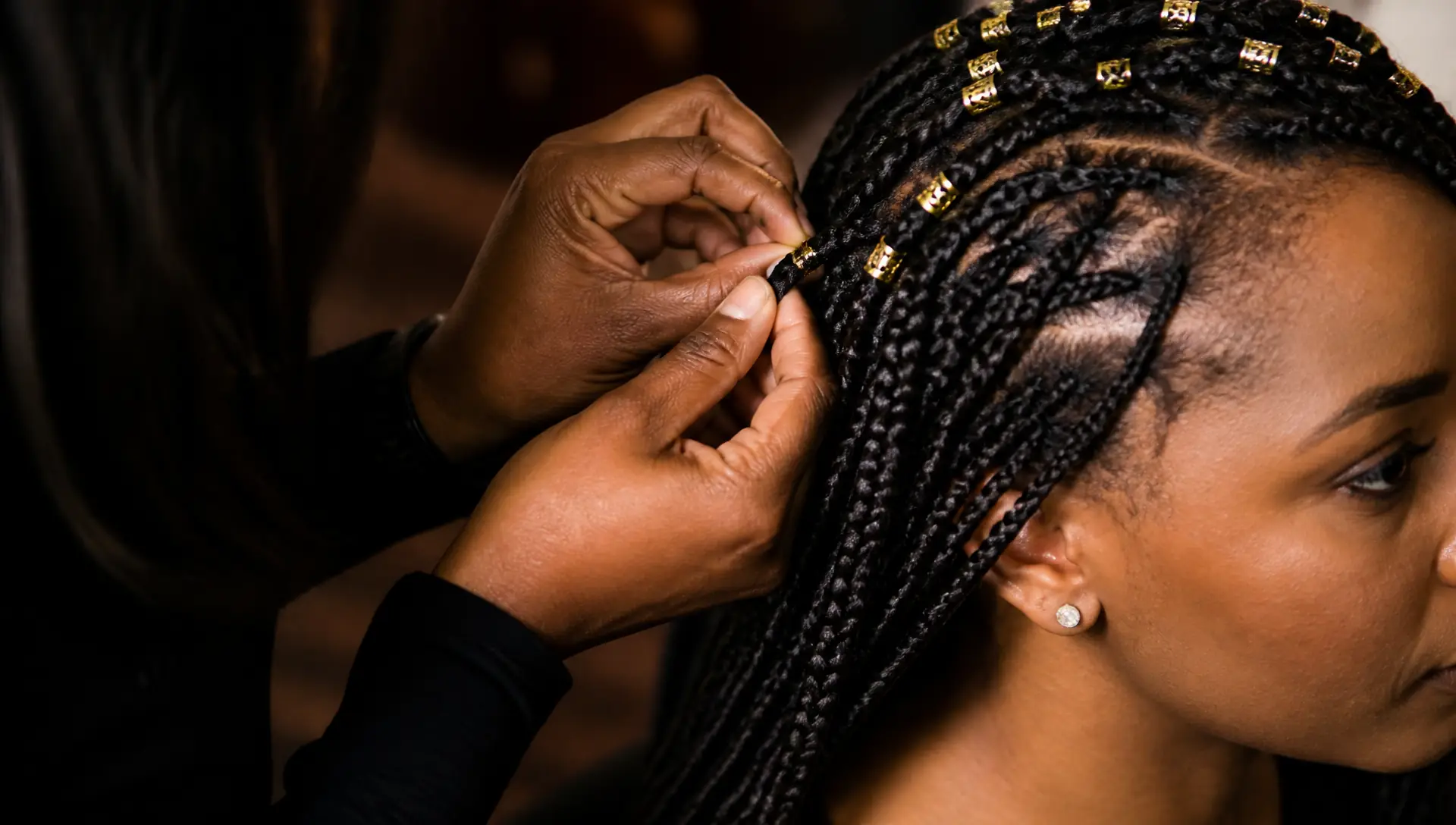 Braider's hands finishing knotless braids with gold cuffs